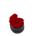 Black heart-shaped box containing six red roses