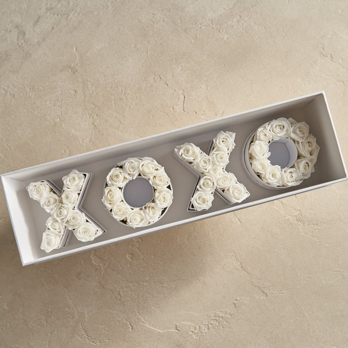 Box containing floral arrangements shaped as the letters X, O, X, O made of white roses.